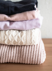 Stack of warm knitted woolen sweaters pastel shades and dark blue on a wood table