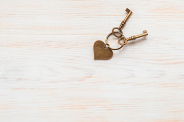 Bronze color keys and heart hitched on ring on wooden board. Space for text.