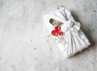 Eco-friendly fabric reusable gift packaging with Eucalyptus, white flowers and red wood heart. Valentine's day reusable sustainable gift wrapping alternative. Zero waste concept.