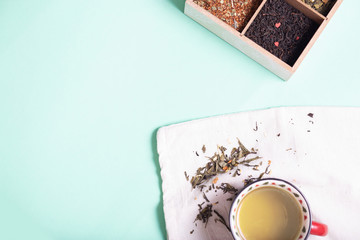 4 types of leaf tea of ​​green, black, herbal with flowers and hearts in a tea box and a mug of black tea on a light background with copy space, top view
