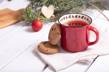 red christmas mug with tea, homemade cookies and fir branches on a light background