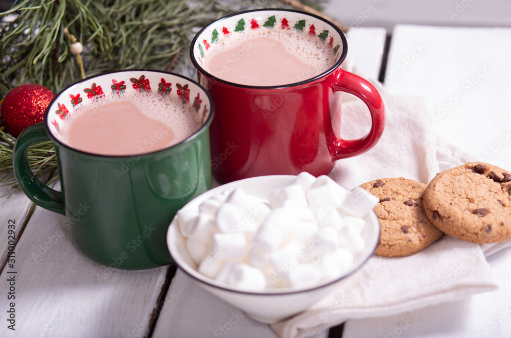 Wall mural two mugs red and green with hot chocolate and marshmallows on a saucer, homemade cookies and fir branches on a light background