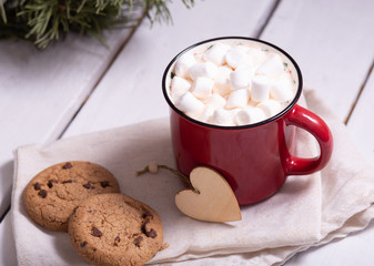 two mugs red and green with cocoa and marshmallows, homemade cookies on a napkin, spruce branches on a light background, top view