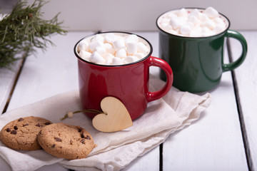 two mugs red and green with cocoa and marshmallows, homemade cookies on a napkin on a light background, top view