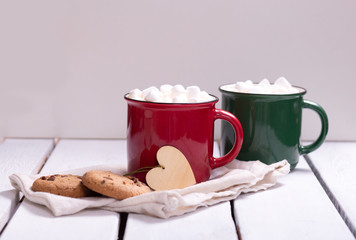 two mugs red and green with cocoa and marshmallows, homemade cookies on a napkin on a light background, top view