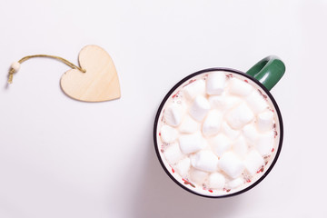 green mug with hot chocolate and marshmallows, Christmas tree decoration - a heart of wood on a light background, top view,