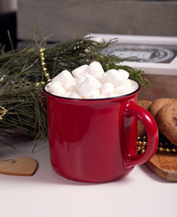 Fototapeta na wymiar Red mug with cocoa and marshmallows stands on a New Year's table, cookies on a wooden board, coniferous branches, close-up