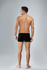 Handsome man in black underwear on light grey background, back view