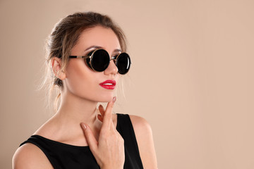 Young woman wearing stylish sunglasses on beige background. Space for text
