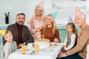 happy family smiling at camera while sitting at kitchen table near birthday cake