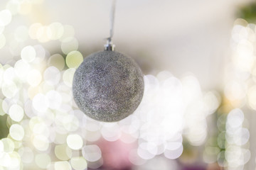 silver bauble hanging on unfocused background with shiny sparkling garland lights and bokeh. Christmas tree toys and New Year decorations.  Winter holidays miracle. Copy space.