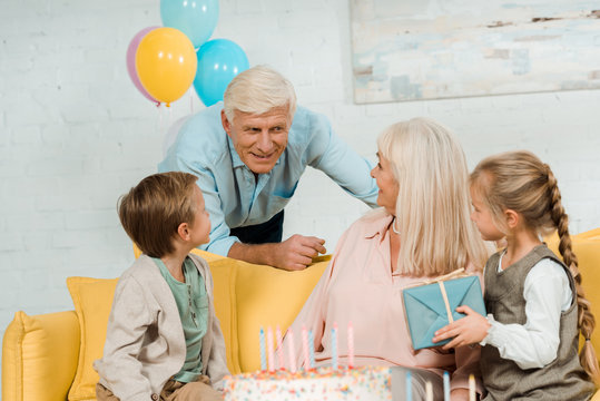 smiling senior man talking to happy wife sitting on sofa with grandchildren