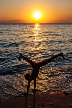 Silhouette of young gymnast woman doing handspring on sandy beach at sunset. Happy child doing cartwheel on the sunny beach sand 