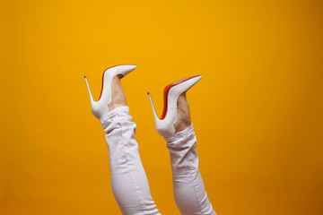Female feet in beautiful white stiletto shoes, yellow background copy space.