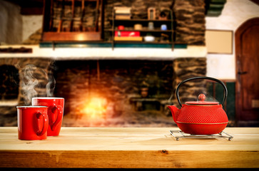Metal kettle on wooden table.Free space for your decoration.Blurred background of fireplace with orange fire. Cold december night in home interior.Hot drink of tea,coffee or mulled.