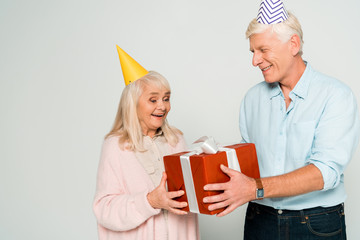 cheerful senior husband and wife holding red gift box isolated on grey