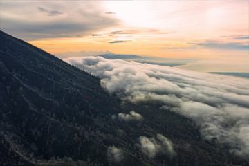Fototapeta premium Stunning aerial view of a mountain surrounded by clouds during sunrise in the Ijen Volcano complex. The Ijen volcano complex is a group of composite volcanoes located in East Java, Indonesia.