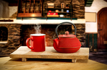 Metal kettle on wooden table.Free space for your decoration.Blurred background of fireplace with orange fire. Cold december night in home interior.Hot drink of tea,coffee or mulled.