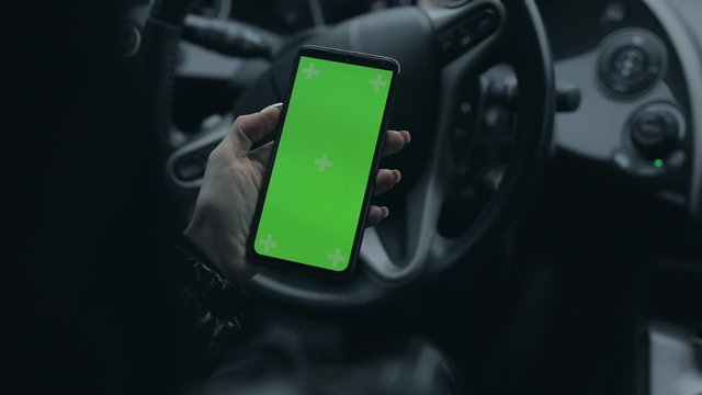 Female hand holding blank green screen of smartphone in a car, chroma key