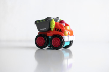 Plastic dump truck toy construction vehicle isolated on white background with reflection. Dumper side view. Orange vehicle with red wheels and name text. Operator in red hard hat