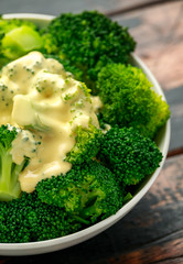 Broccoli with cheese sauce in white bowl on wooden table