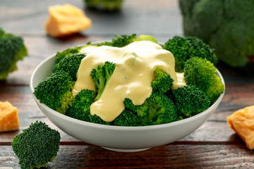 Broccoli with cheese sauce in white bowl on wooden table