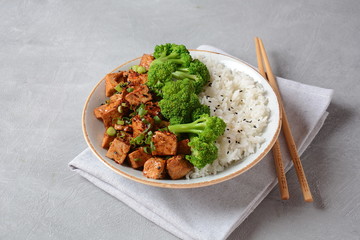 Sweet, spicy , crispy and fried Tofu in teriyaki sauce served in a bowl with broccoli, sesame seeds and rice. Healthy vegan food, gluten-free