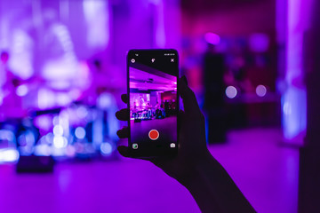 female hand holds a smartphone. records a concert of his favorite group at the club. night life
