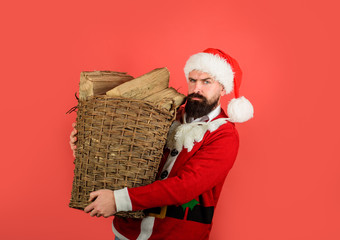 Santa man. Winter holiday vacation. Basket of chopped firewood for heating in winter. Bearded man in Santa claus costume carries wicker basket filled with firewood. Merry Christmas and happy New year.