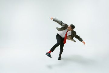 Fototapeta na wymiar Young caucasian man moving flexible on white studio background. Male model in office attire bending over, avoiding something, catched in motion and action. Looks angry, scared, fighting. Emotions.