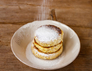 Russian traditional breakfast cottage cheese pancake in plate with sugar powder on wooden background