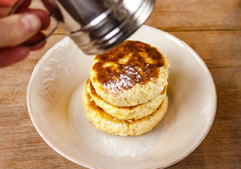 Russian traditional breakfast cottage cheese pancake in plate with sugar powder on wooden background