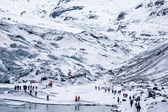 Groups Of Hiking Tourists Trekking In The Snowy White Rugged Mountains