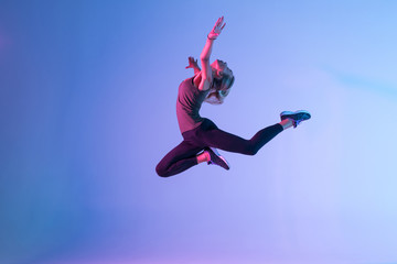 Handsome woman with perfect body jumping against colorful trendy background. Young athletic girl in...