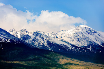 high tatras mountain ridge in springtime. snow capped rocky peaks in dramatic dappled sunlight beneath a clouds on a blue sky. place where earth meets sky concept