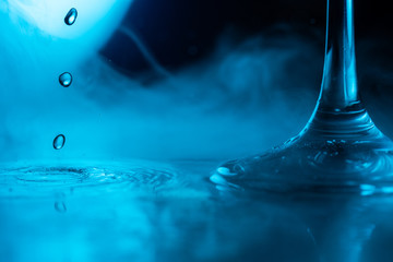 a glass with which drops are dripping stands in a tupan on a blue background