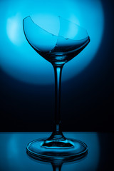 broken glass stands on a glass mirror table illuminated by a round blue lamp