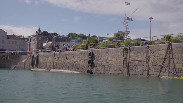 Wide low angle sunny day dolly shot of harbour wall with hanging tyres, landscape coastal buildings, Europe