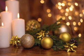 Fototapeta na wymiar Golden Christmas ball on a tree branch, white candle flame with stars bokeh lights on a brown background 2020