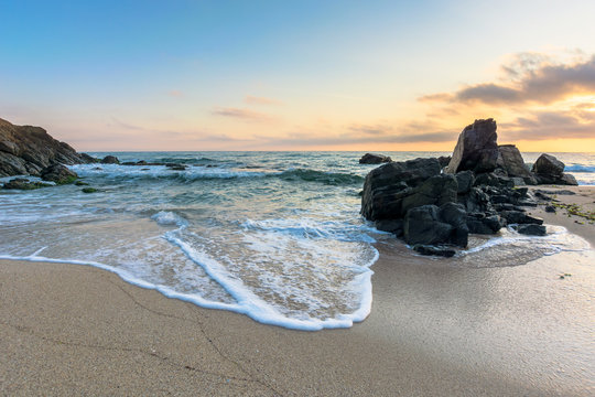 sea beach at sunrise. calm waves wash huge rocks. golden clouds on the sky. stunning marine scenery in morning light.