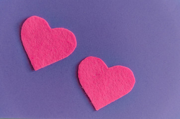 Pink felt hearts with green clothespins on a purple background. St. Valentine's Day and romance concept. Top view, flat lay. Copy space.