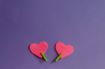 Fototapeta premium Pink felt hearts with green clothespins on a purple background. St. Valentine's Day and romance concept. Top view, flat lay. Copy space.