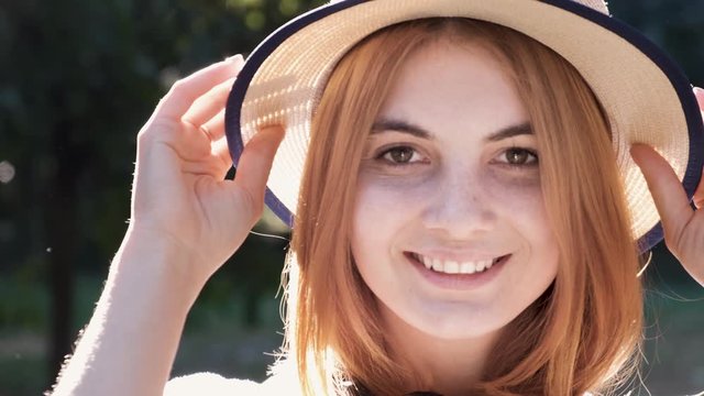 Portrait of pretty positive teenage girl with red hair wearing straw hat and pink earphones smiling happily in camera.