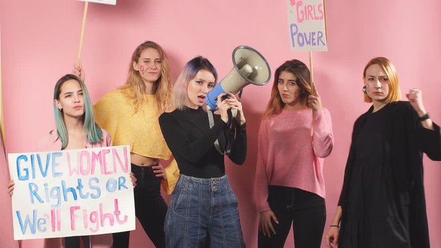Active promotion of feminism by young caucasian girls isolated over pink background, using megaphones and poster with inscriptions. Confident and independent girls feminists
