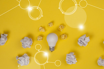 new idea concept with crumpled office paper and white light bulb on yellow background. Creative solution during brainstorming session concept. Flat lay, top view, copy space