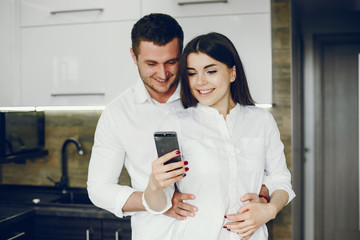 Cute couple on a kitchen. Pretty brunette in a white shirt. Man and woman use the phone
