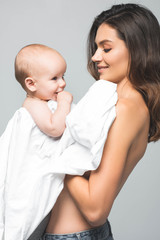portrait of cheerful naked mother holding baby boy, isolated on grey