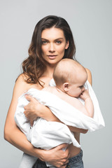 portrait of attractive naked mother holding baby boy, isolated on grey