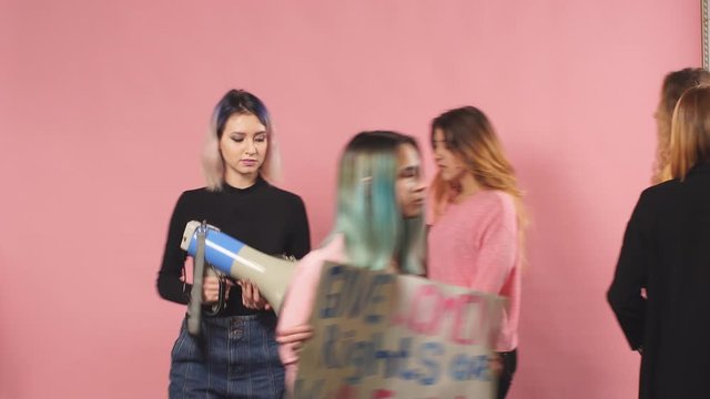 Portrait of young confident women fighting for women rights holding posters with inscriptions isolated over pink background, independence and feminism concept