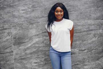 Cute black girl near gray wall. Lady in a white t-shirt and blue jeans.